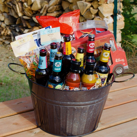 Beer gift basket calgary local beer bottles gourmet nut mixes hot sauce doritos pretzels all in a metal tin sitting on a picnic table