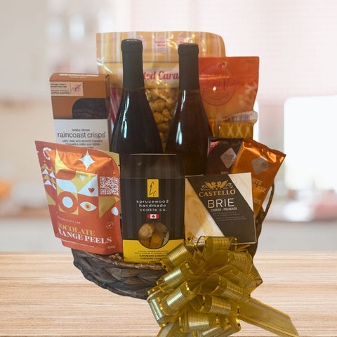 Gourmet gift basket with wine, snacks, and a bow on a wooden surface.